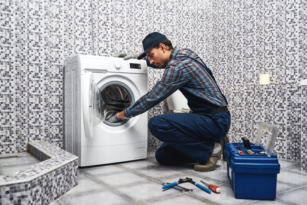 Washing mashine is leaked. Working man plumber repairs a washing machine